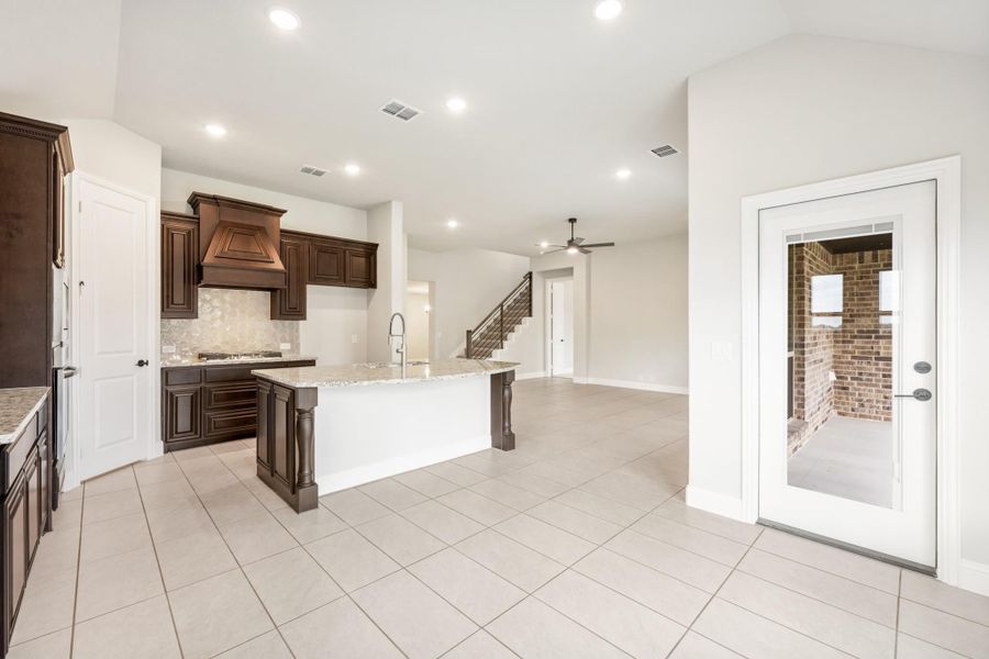 Open kitchen with dark wood cabinets, large island, and tile floors opening to living area with staircase Open kitchen with dark wood cabinets, large island, and tile floors opening to living area with staircase
