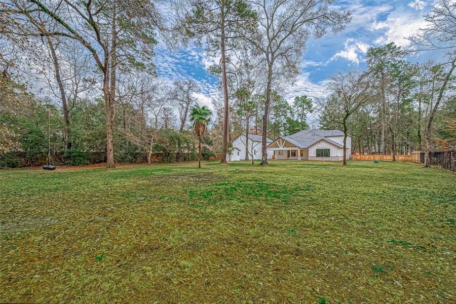 Spacious backyard with mature trees, a tire swing, and a large lawn.