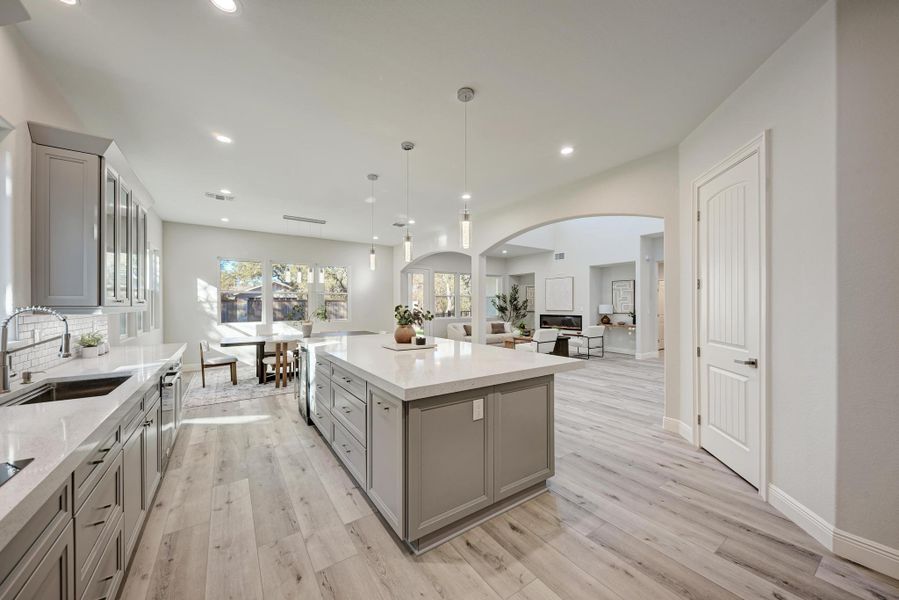 Kitchen featuring gray cabinets, arched walkways, open floor plan, a kitchen island, and pendant lighting