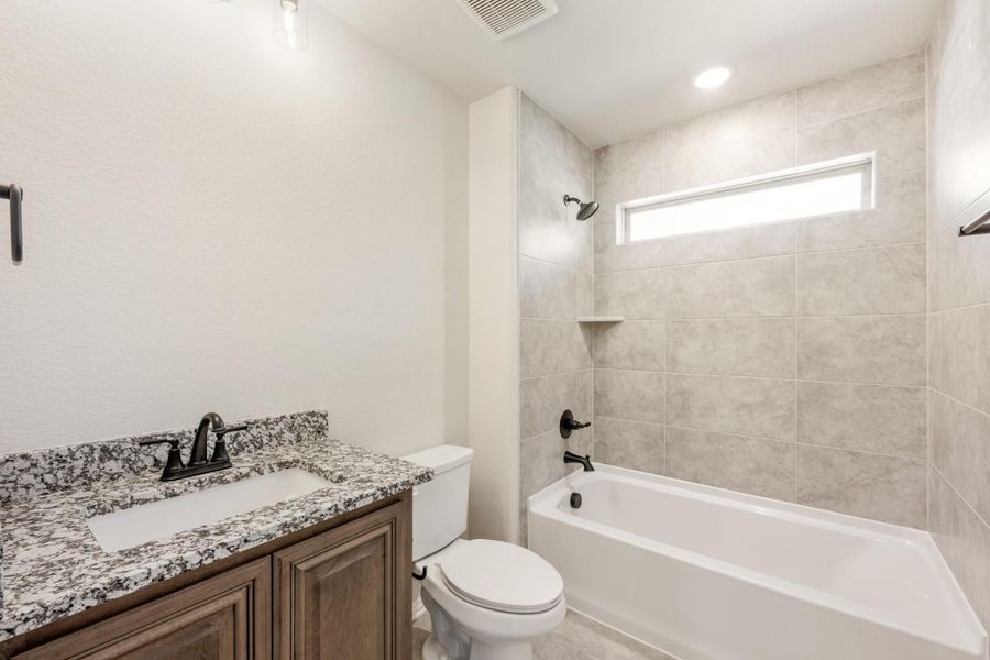 Bathroom with granite vanity, wood cabinets, and tiled tub-shower combo with small window