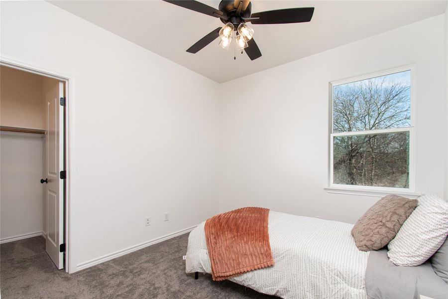 Carpeted bedroom with a spacious closet and ceiling fan