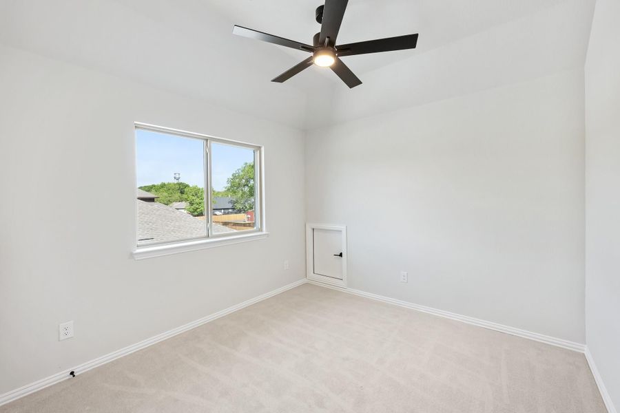 Empty bedroom with carpet flooring, black ceiling fan, and a window with neighborhood view