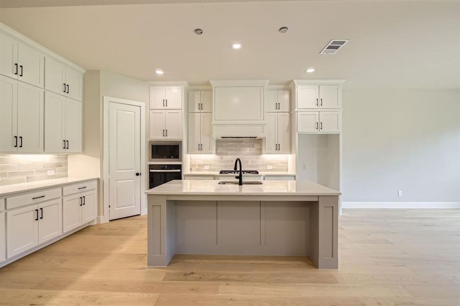 Kitchen with built in microwave, black oven, tasteful backsplash, white cabinets, and recessed lighting Kitchen with built in microwave, black oven, tasteful backsplash, white cabinets, and recessed lighting