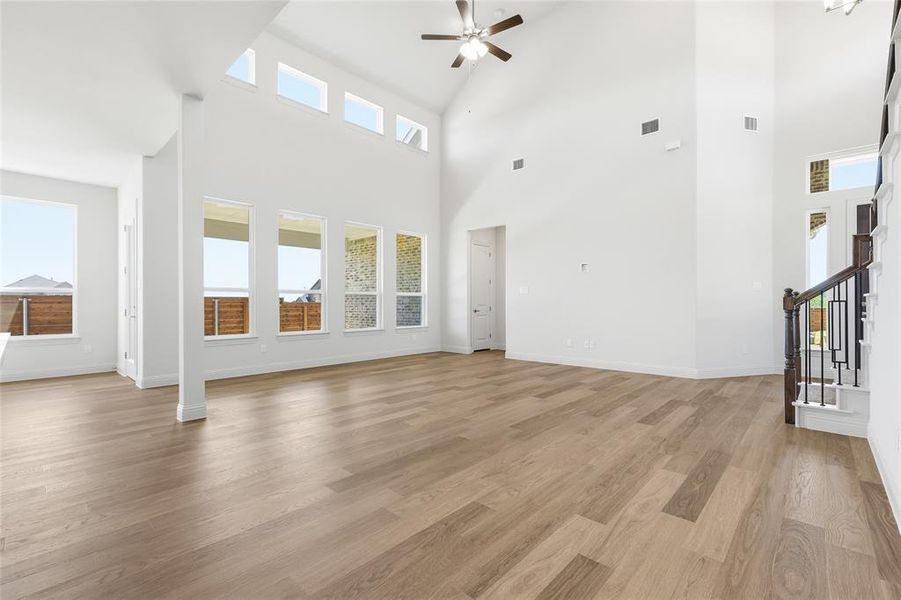 Unfurnished living room featuring ceiling fan, light wood-style flooring, and a high ceiling