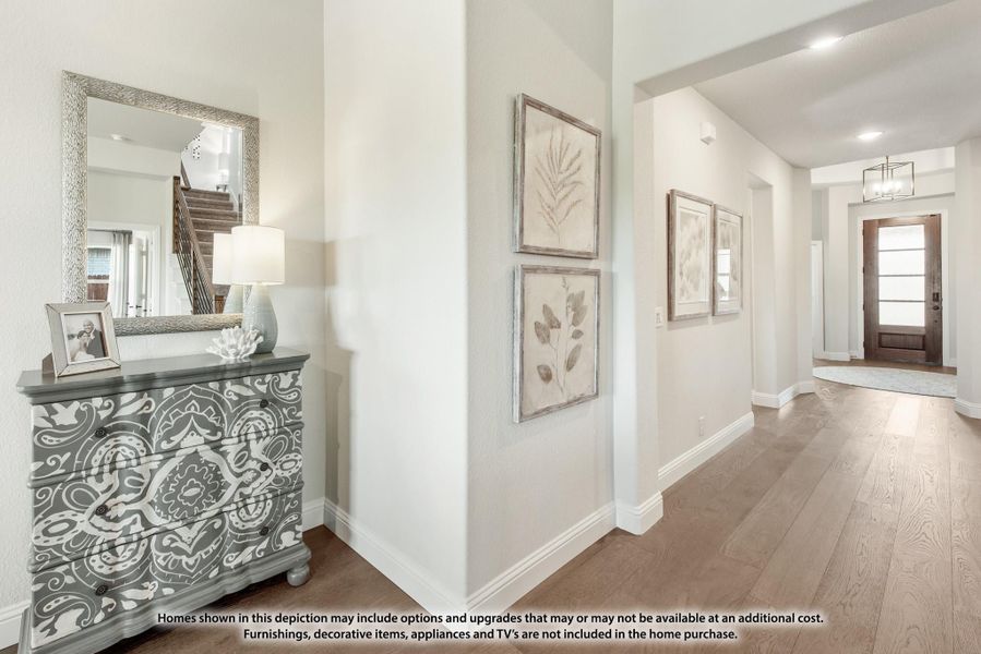 Bright entryway hallway with hardwood floors, framed wall art, decorative dresser with mirror, and wood front door.