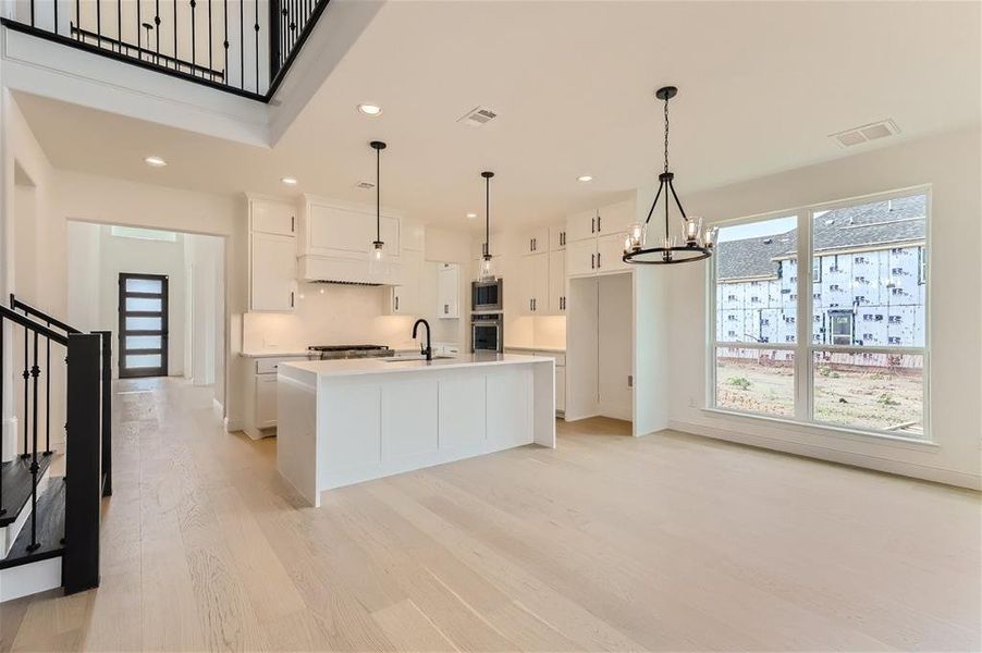 Kitchen featuring hanging light fixtures, white cabinets, light wood-type flooring, and stainless steel oven