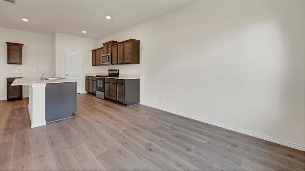 Spacious kitchen area featuring an island with a sink, dark wood-finish cabinetry, stainless steel appliances, and light-toned countertops
