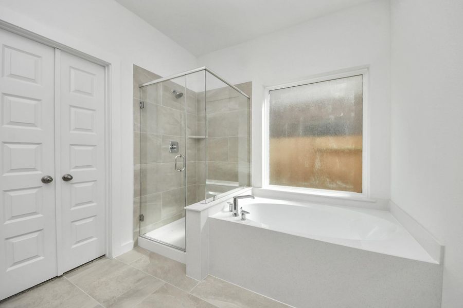Indulge in a spa-like retreat within the confines of this primary bathroom. Delight in a spacious walk-in shower enveloped in stylish tile surround, unwind in a separate garden tub adorned with custom detailing. Sample photo of completed home with similar floor plan. Actual colors and selections may vary.