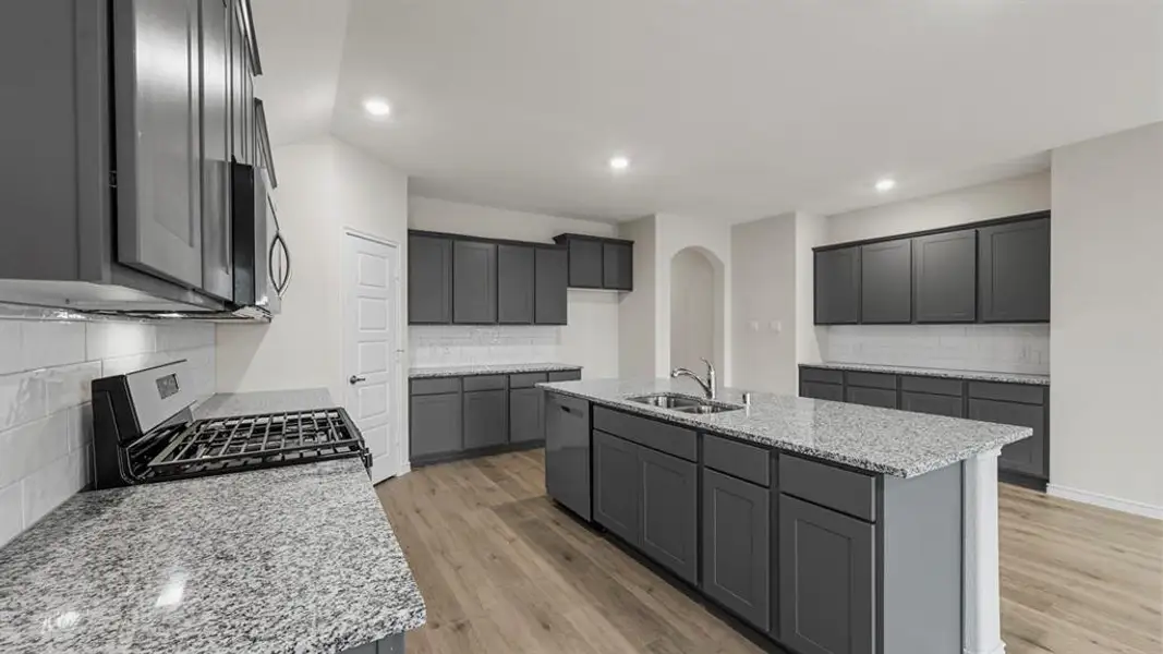 Spacious kitchen featuring an expansive center island, extensive gray cabinetry, light-toned wood-finish flooring, a stainless steel gas range, and speckled countertops