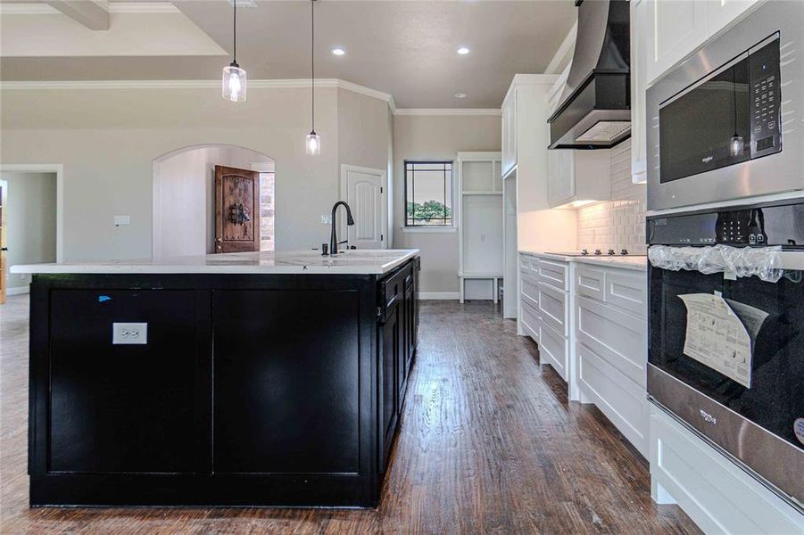 Kitchen featuring white cabinetry, dark hardwood / wood-style flooring, decorative backsplash, custom range hood, and a kitchen island with sink