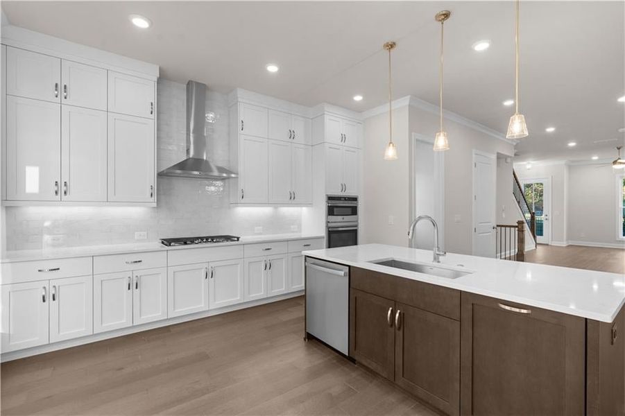 Kitchen featuring white cabinets, light wood-style floors, recessed lighting, hanging light fixtures, and an island with sink