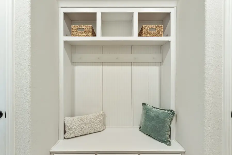 White built-in mudroom nook with bench seat, coat hooks, and upper cubbies holding wicker baskets