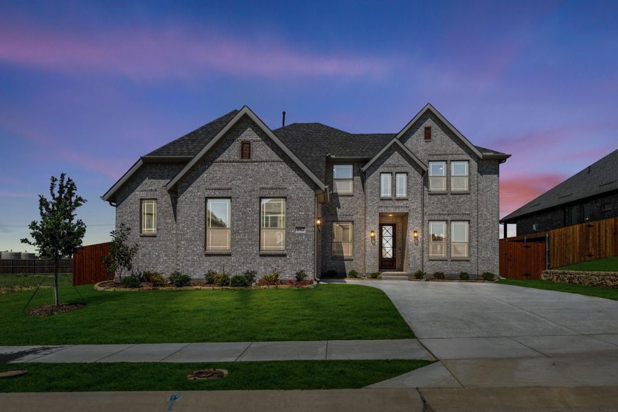 Two-story brick home with dark roof, large windows, and manicured front lawn at dusk Two-story brick home with dark roof, large windows, and manicured front lawn at dusk
