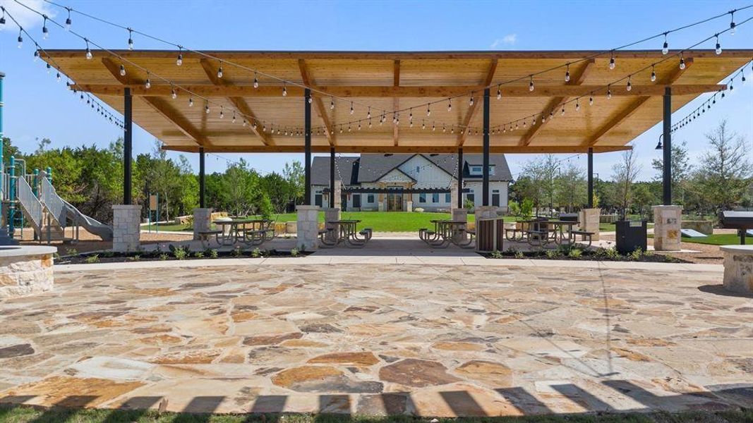 Expansive flagstone patio area with a wooden pergola, string lighting, and multiple picnic tables