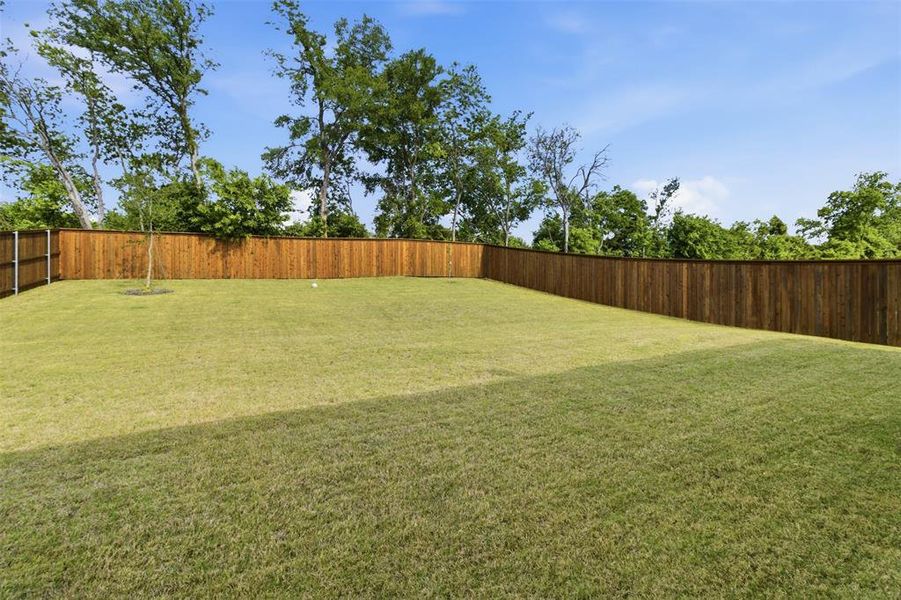 Expansive backyard featuring a lush lawn, privacy fencing, and mature trees along the perimeter