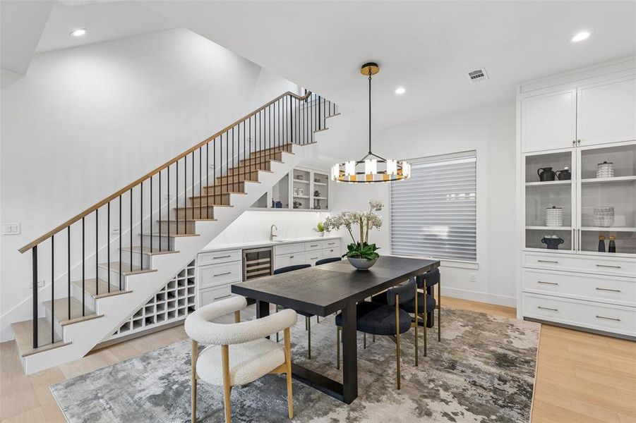 Dining area with designer lighting and built-in bar featuring wine storage and beverage fridge, conveniently tucked beneath the staircase.