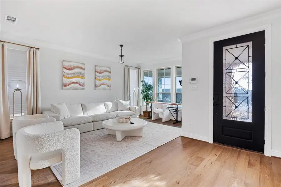 Living room with baseboards, visible vents, ornamental molding, and light wood-style flooring