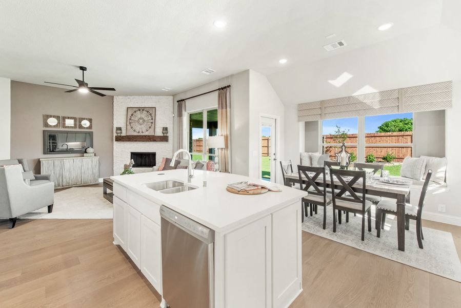Open-concept kitchen with white island, dining area, and living room with brick fireplace and hardwood floors