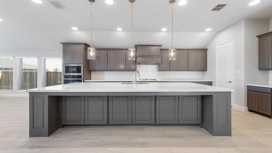 Kitchen featuring appliances with stainless steel finishes, hanging light fixtures, a large island, and sink