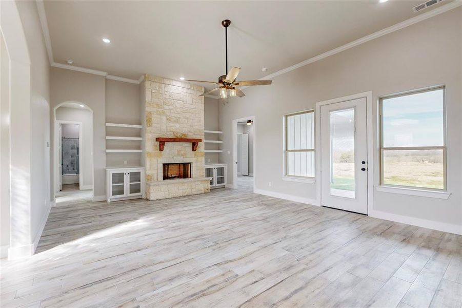 Unfurnished living room with ornamental molding, a stone fireplace, light wood-type flooring, and ceiling fan