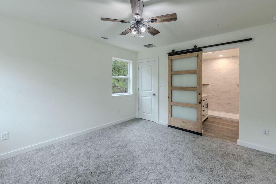 A quiet retreat with plush carpeting and a modern barn door leading to an adjoining bath. A quiet retreat with plush carpeting and a modern barn door leading to an adjoining bath.