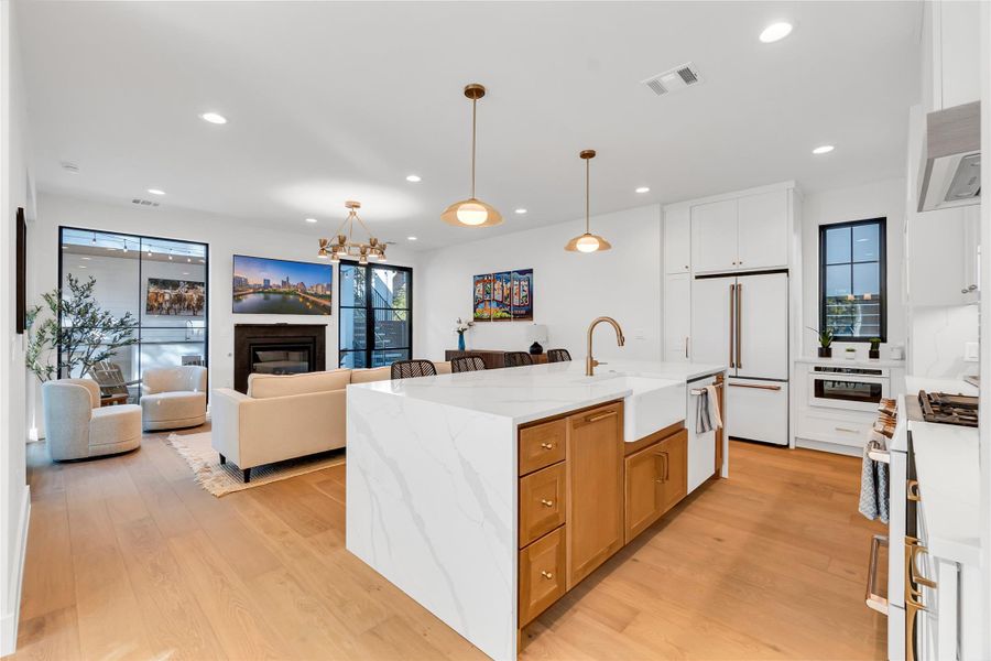 Kitchen with light stone counters, white cabinetry, open floor plan, premium appliances, and a chandelier Kitchen with light stone counters, white cabinetry, open floor plan, premium appliances, and a chandelier