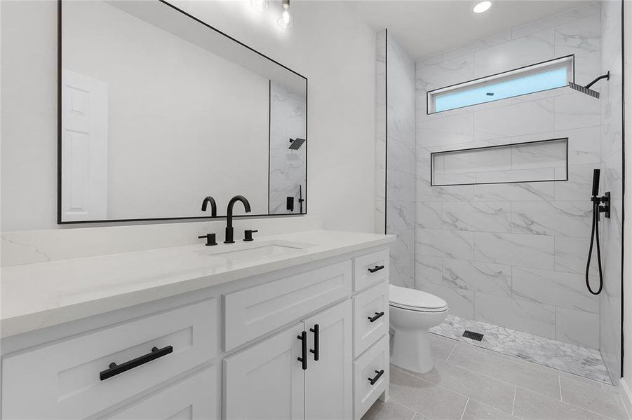 Bathroom featuring tile patterned floors, tiled shower, toilet, and vanity