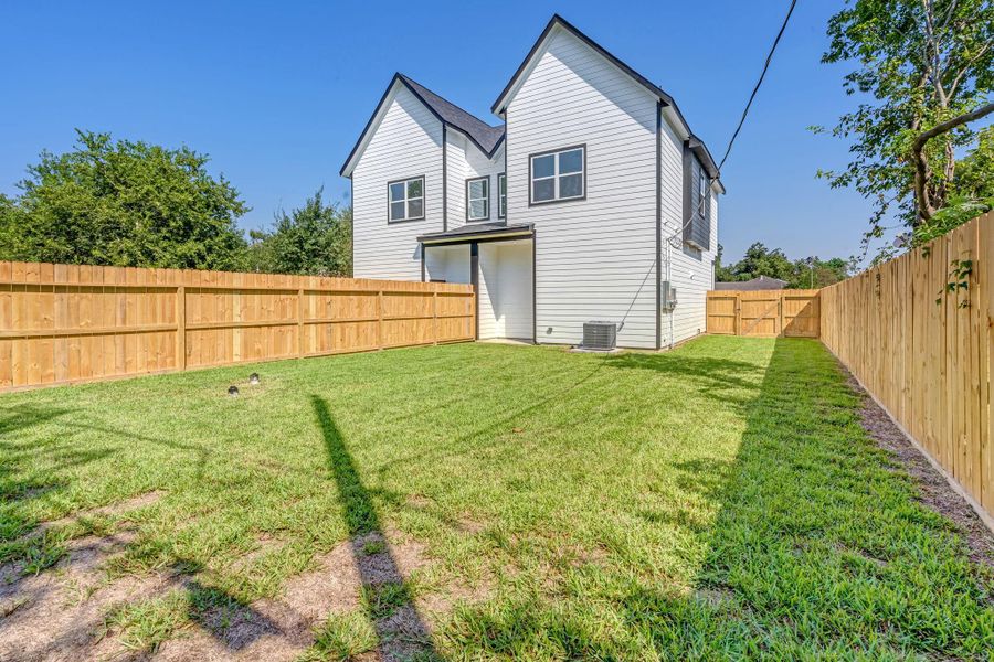 Full backyard view highlighting the home’s covered patio, spacious lawn, and private wood fencing, with a side gate providing convenient access to the yard.