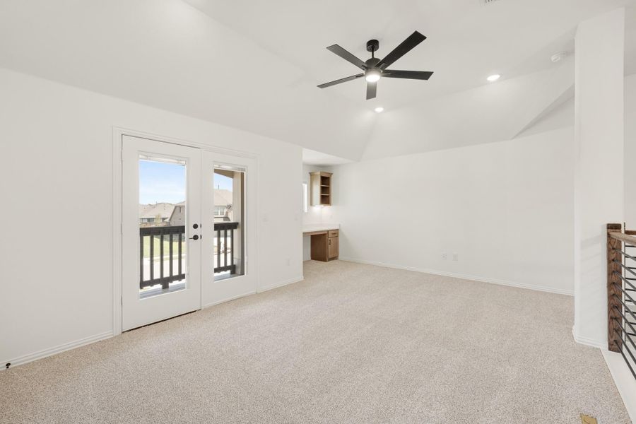 Bonus room with carpet, vaulted ceiling, ceiling fan, French doors to balcony, and built-in desk area