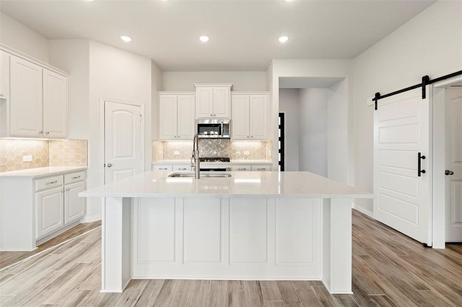 Kitchen with a barn door, white cabinetry, light stone counters, recessed lighting, and light wood-type flooring
