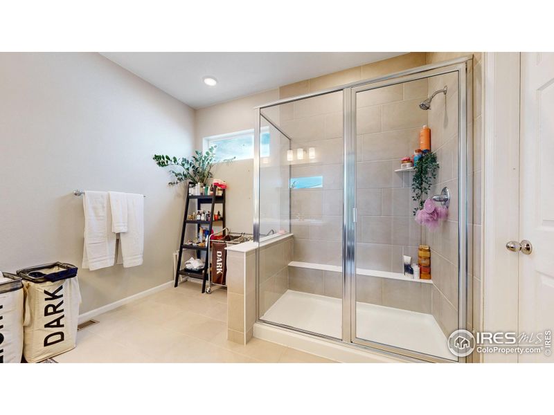 Primary bathroom featuring quartz countertops, dual vanities, a walk-in shower and a large walk-in closet.