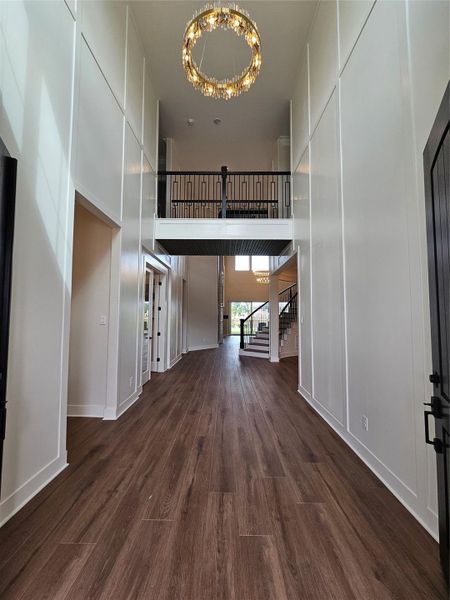 Spacious entryway with high ceilings, elegant chandelier, and dark wood flooring. Features a modern staircase and a second-floor balcony, creating a grand and open feel. Spacious entryway with high ceilings, elegant chandelier, and dark wood flooring. Features a modern staircase and a second-floor balcony, creating a grand and open feel.