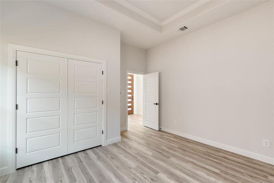 Second bedroom featuring a raised ceiling, light wood finished floors, a closet, and crown molding