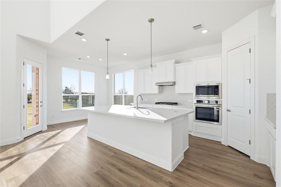 Kitchen featuring white cabinetry, an island with sink, stainless steel appliances, decorative backsplash, and dark wood-style floors Kitchen featuring white cabinetry, an island with sink, stainless steel appliances, decorative backsplash, and dark wood-style floors