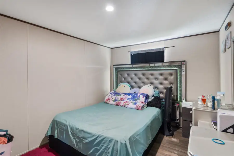 Recessed lighting overhead illuminates a cozy bedroom featuring smooth walls and durable wood flooring.