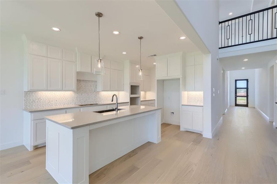 Kitchen with an island with sink, white cabinetry, sink, and backsplash