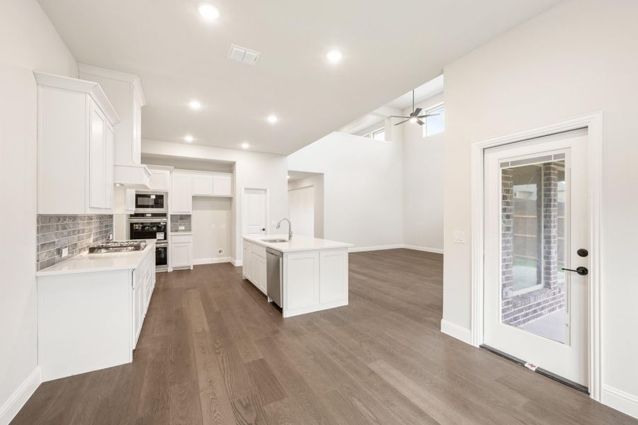 Open kitchen with white cabinets, center island, stainless appliances, gray tile backsplash, and dark hardwood floors Open kitchen with white cabinets, center island, stainless appliances, gray tile backsplash, and dark hardwood floors