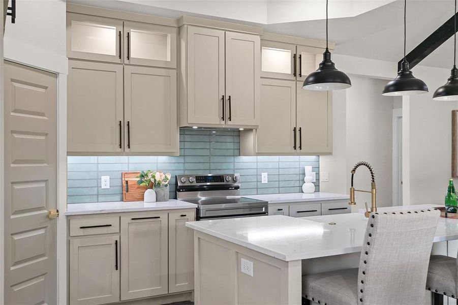 Modern kitchen featuring light cabinetry with black hardware, a blue tile backsplash, stainless steel range, and a kitchen island with a gold-tone faucet Modern kitchen featuring light cabinetry with black hardware, a blue tile backsplash, stainless steel range, and a kitchen island with a gold-tone faucet