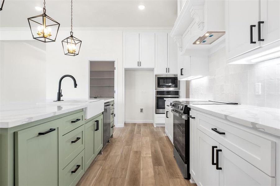 Kitchen with white cabinets, green cabinetry, appliances with stainless steel finishes, a center island with sink, and light stone countertops