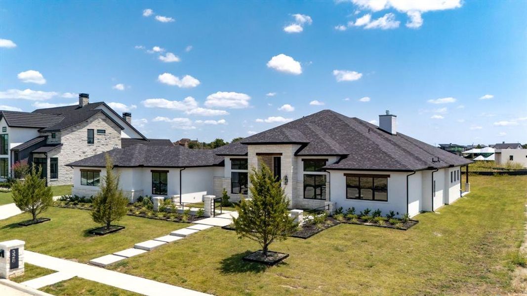 Transtional home with a front yard, roof with shingles, stucco siding, and stone siding