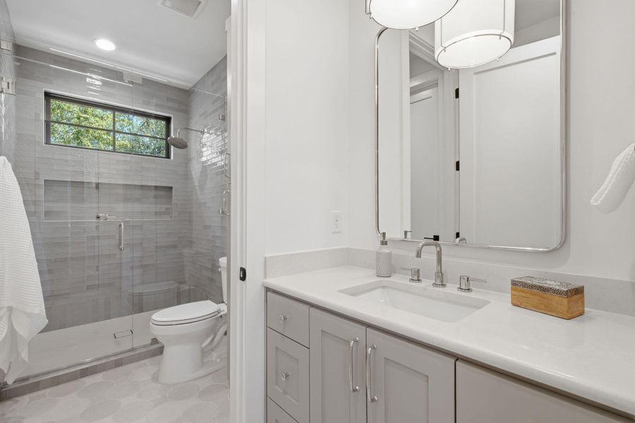 An elegant walk-in glass shower anchors this modern bathroom with a stone-counter vanity.