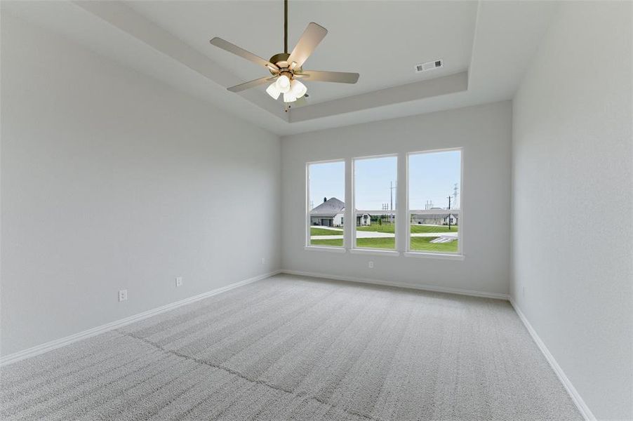 Spacious room with light-colored carpeting, three windows, and a ceiling fan