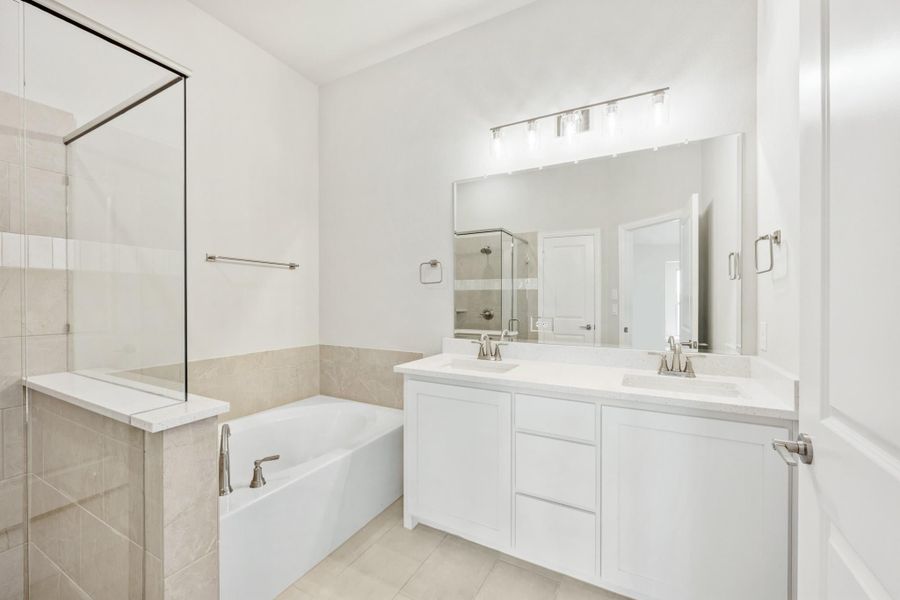 Bathroom with double vanity, soaking tub, glass shower, white cabinets, and large mirror with overhead lighting Bathroom with double vanity, soaking tub, glass shower, white cabinets, and large mirror with overhead lighting