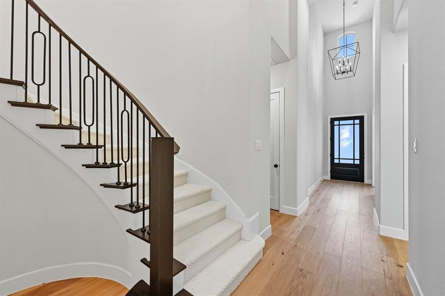 Entryway featuring light wood finished floors, healthy amount of natural light, a towering ceiling, stairway, and a chandelier