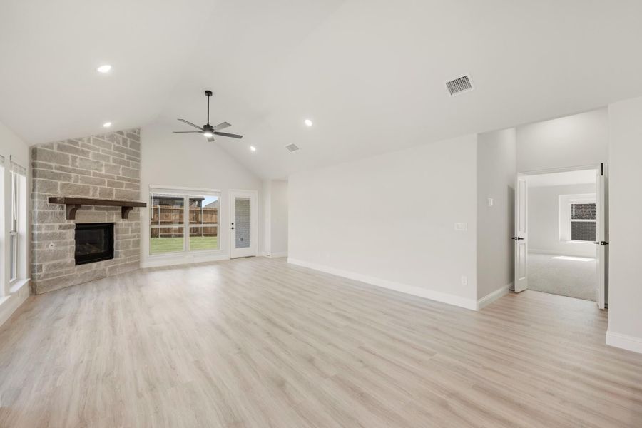 Open living room with vaulted ceiling, stone fireplace, ceiling fan, and light wood floors
