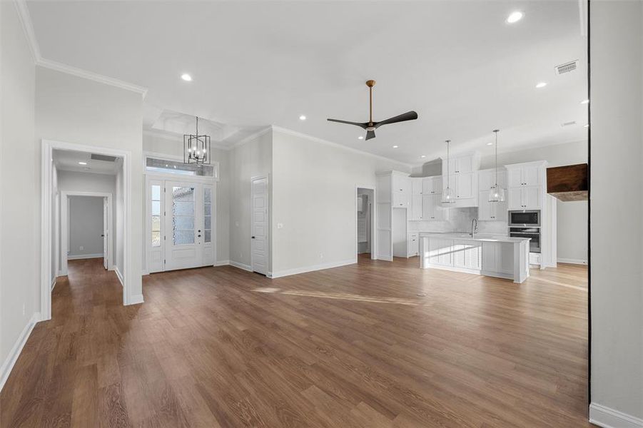 Unfurnished living room featuring a ceiling fan, dark wood-style flooring, a chandelier, recessed lighting, and ornamental molding Unfurnished living room featuring a ceiling fan, dark wood-style flooring, a chandelier, recessed lighting, and ornamental molding