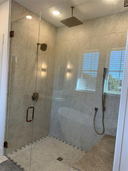 Glass-enclosed shower with large format tile walls, a mosaic tile floor, and a stone bench