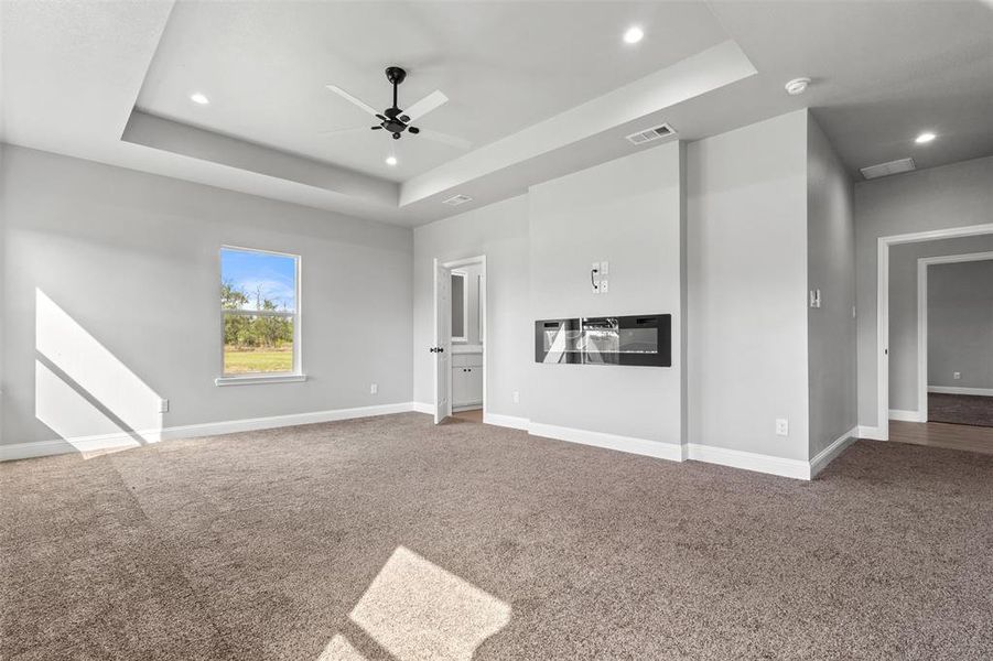 Unfurnished living room featuring carpet floors, a raised ceiling, ceiling fan, and recessed lighting