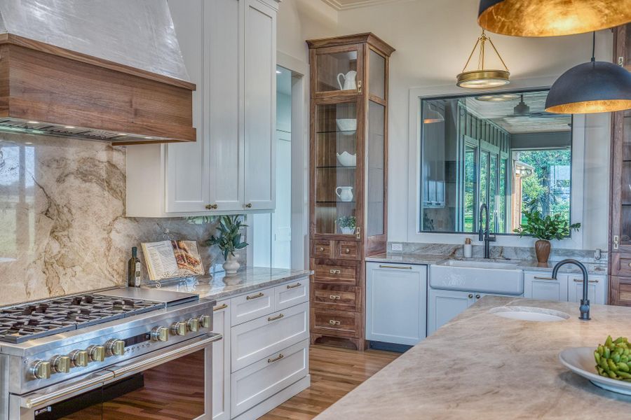 Kitchen with high end stainless steel range oven, custom exhaust hood, tasteful backsplash, glass insert cabinets, and white cabinetry Kitchen with high end stainless steel range oven, custom exhaust hood, tasteful backsplash, glass insert cabinets, and white cabinetry