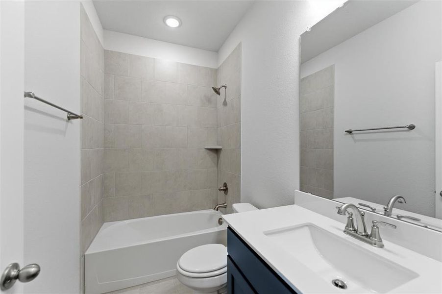 Bathroom featuring a white bathtub, gray tiled shower surround with a built-in niche, and a vanity with a white countertop and dark blue cabinetry